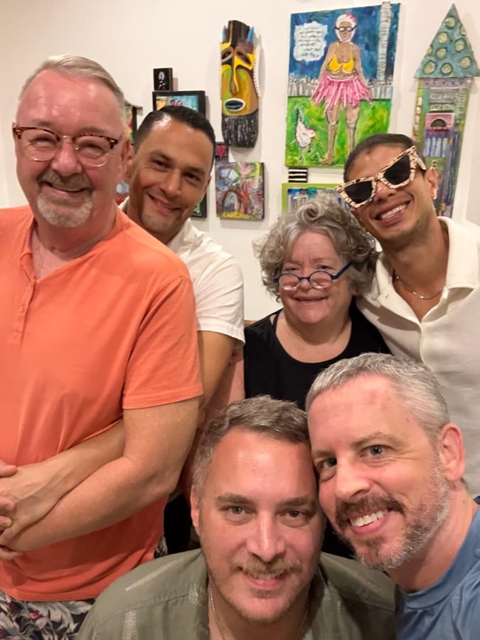 Six friends squeezed into a group photo in a room hung with bright folk art