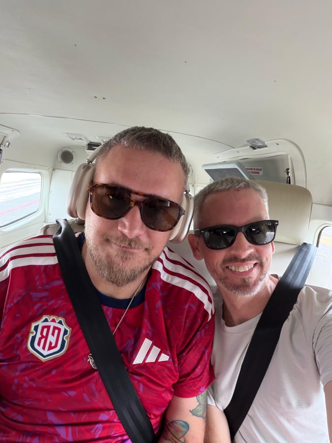 Two of us buckled into a small propeller plane, one wearing a Costa Rica football shirt