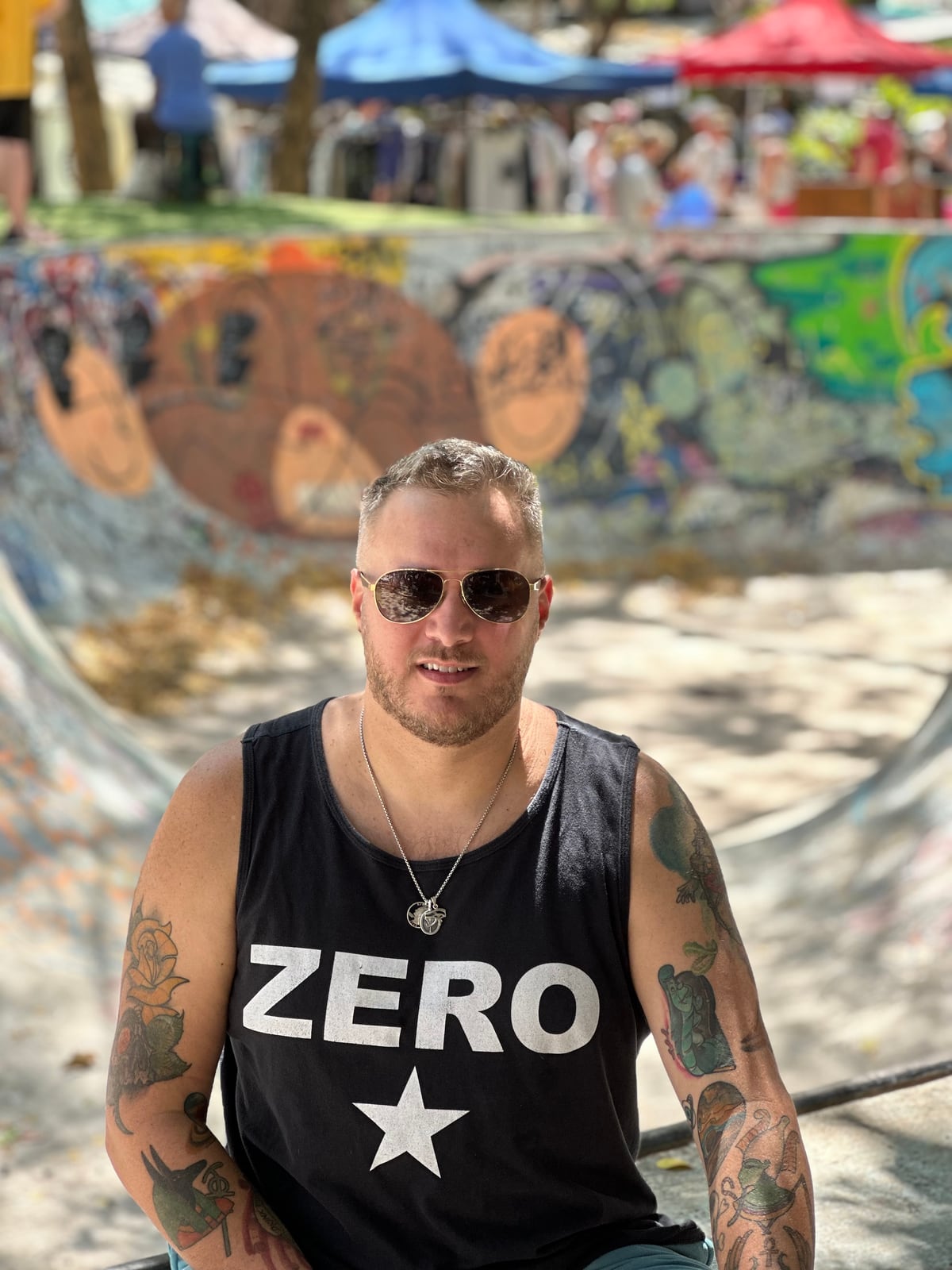 Robbie Parker sitting in front of a graffiti-covered skate bowl, in sunglasses and a black vest